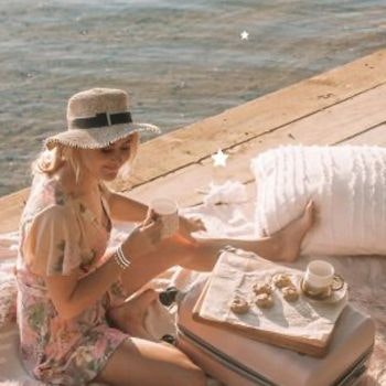 Girl in a sunhat having a picnic on the pier with her dusty pink suitcase