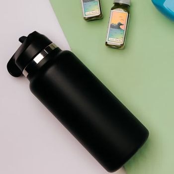 Black hydro flask flat lay with green juice bottles