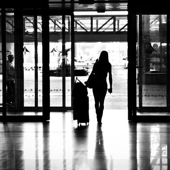 A silhouette of a woman walking through the airport with her suitcase and a duffle bag