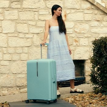 Woman in a sundress with her Samsonite Hi-Fi suitcase outside brick building