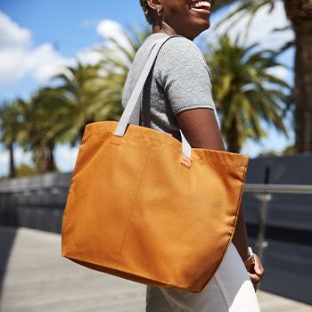 Bellroy Market Tote in caramel worn by a woman outside, with palm trees behind her