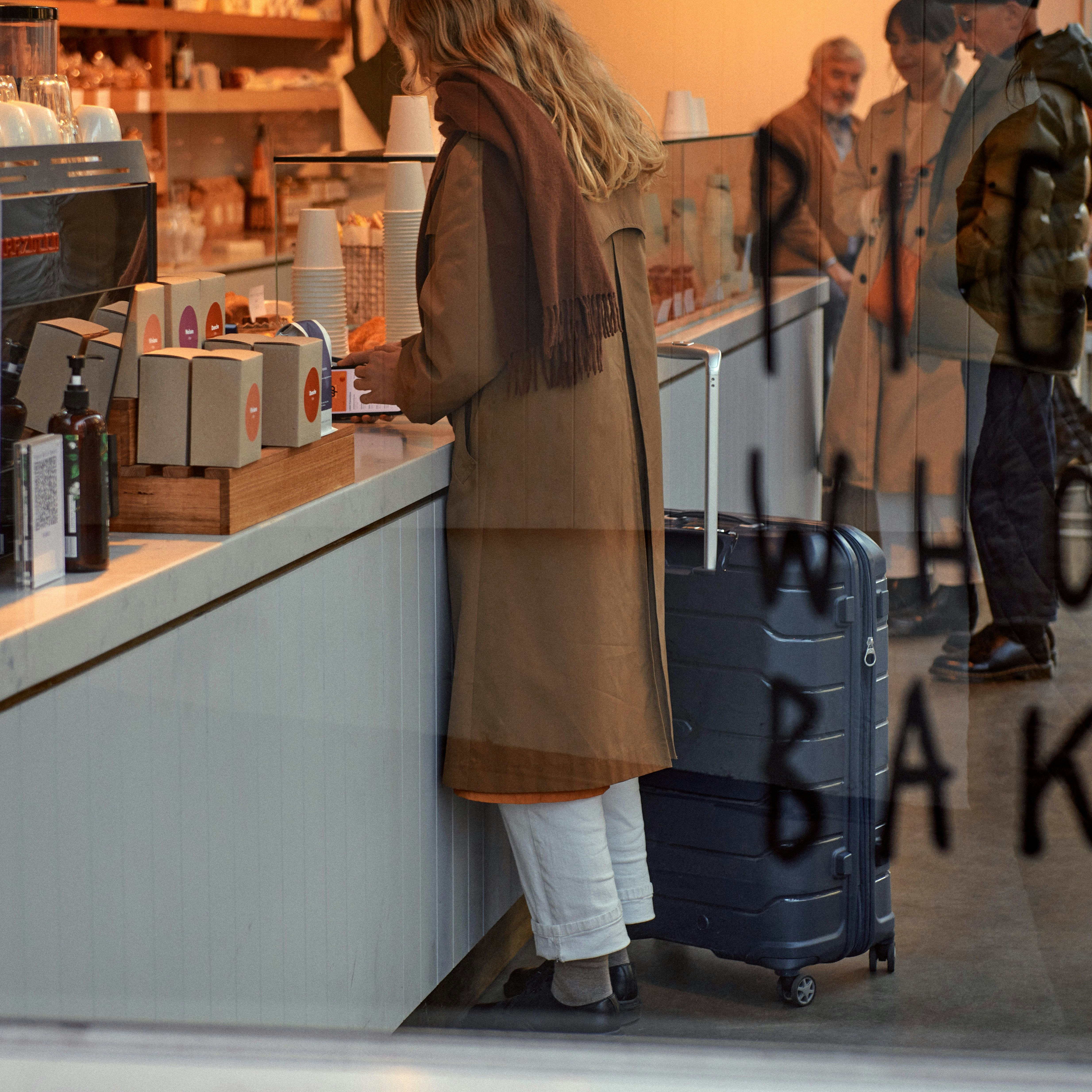 Looking through a window of a woman at the counter of a coffee shop / bakery with a Samsonite Oc2lite in tow