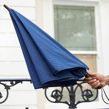 Navy Blunt Umbrella being held when shut outside a building
