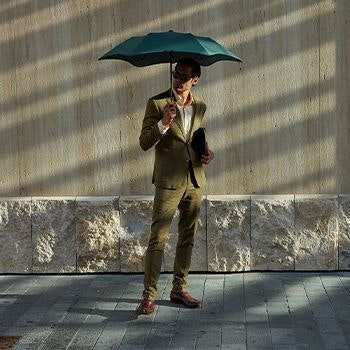 Man holding a green blunt umbrella outside, wearing a green suit